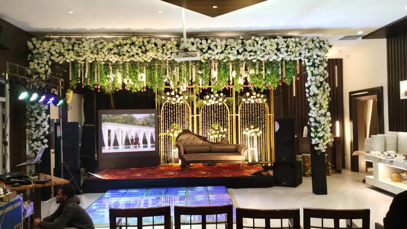 Air-conditioned banquet hall interior with a decorated floral stage and LED dance floor